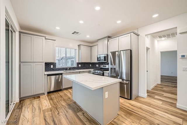 kitchen featuring light wood-style floors, light stone countertops, gray cabinetry, appliances with stainless steel finishes, and decorative backsplash