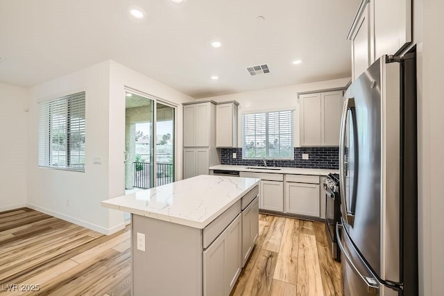 kitchen with freestanding refrigerator, gray cabinets, light wood-style flooring, and gas stove