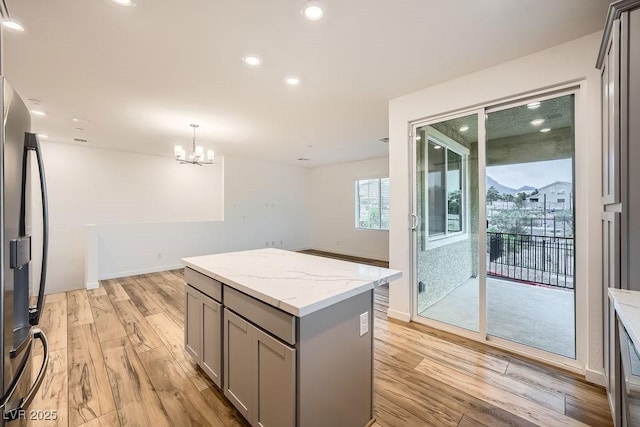kitchen featuring an inviting chandelier, stainless steel fridge, a center island, light wood-style flooring, and gray cabinets