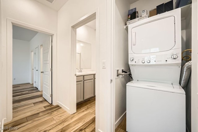laundry area featuring a sink, stacked washer / dryer, laundry area, light wood finished floors, and baseboards