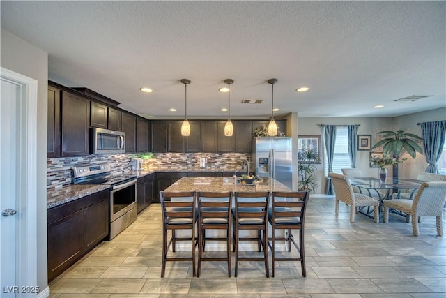 kitchen featuring tasteful backsplash, dark brown cabinetry, stone counters, a kitchen breakfast bar, and stainless steel appliances