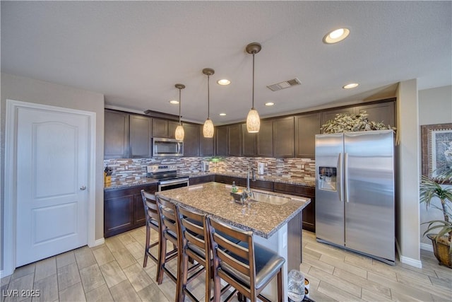 kitchen with visible vents, a sink, stainless steel appliances, light stone countertops, and dark brown cabinets