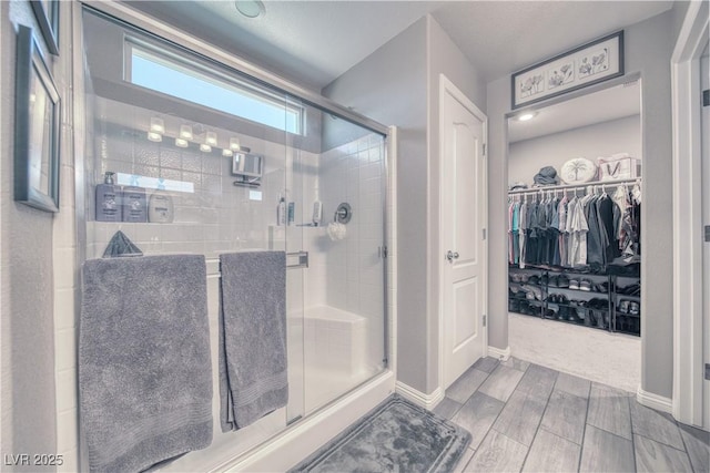 bathroom featuring a walk in closet, baseboards, wood tiled floor, and a shower stall