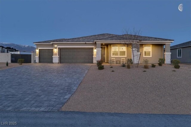 prairie-style home featuring stucco siding, decorative driveway, a garage, and fence