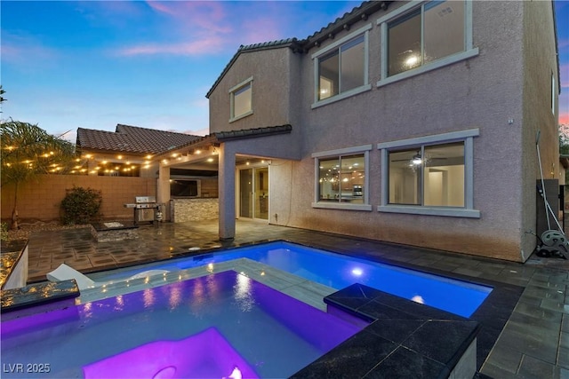 back of property at dusk with fence, stucco siding, a patio area, and a tiled roof