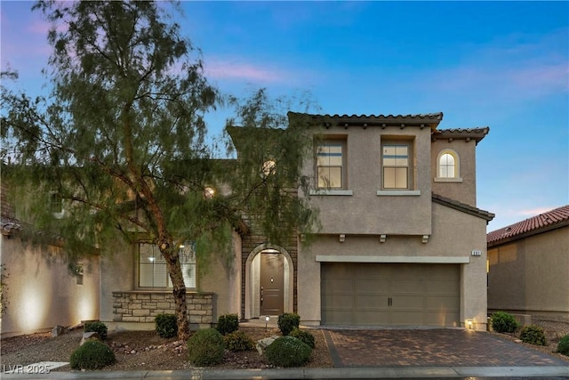 mediterranean / spanish-style home featuring an attached garage, decorative driveway, stucco siding, and a tiled roof