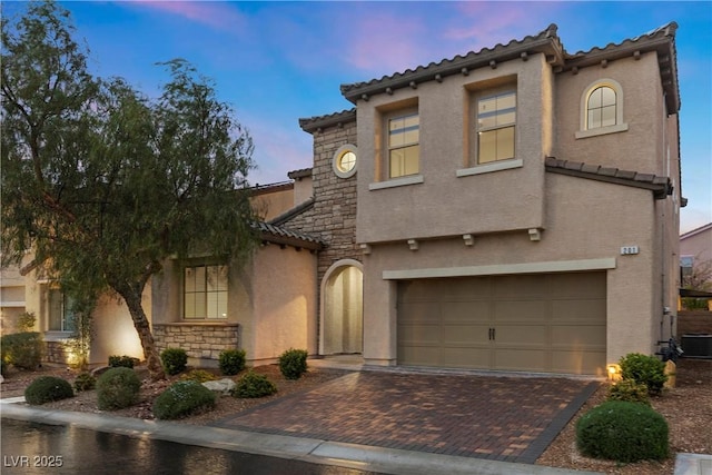 mediterranean / spanish-style house with stone siding, a garage, stucco siding, decorative driveway, and a tiled roof