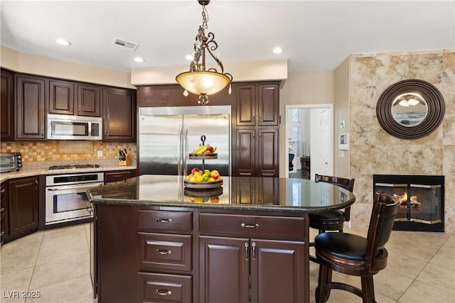 9517 Spanish Steps Ln, Las Vegas, NV 89117 - kitchen featuring appliances with stainless steel finishes, light tile patterned floors, a breakfast bar area, dark stone counters, and recessed lighting