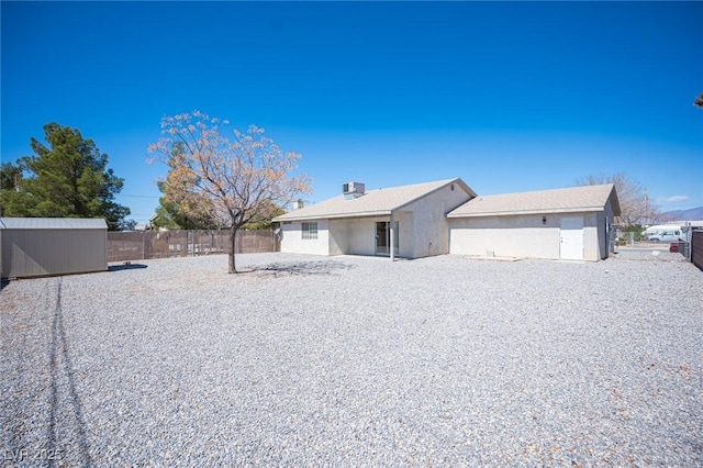 view of front facade featuring stucco siding, a storage unit, an outdoor structure, and fence