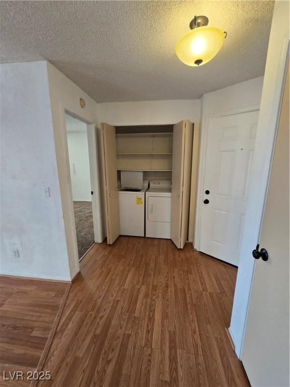 clothes washing area with independent washer and dryer, laundry area, wood finished floors, and a textured ceiling