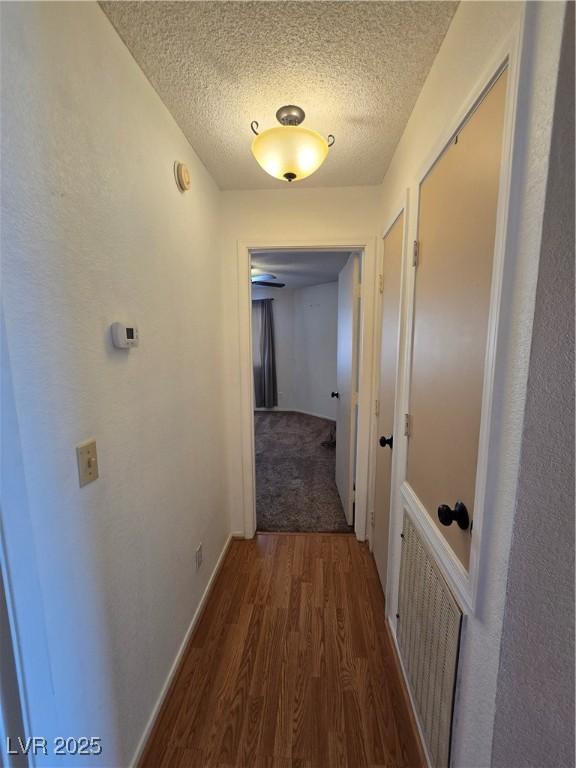 hallway featuring visible vents, a textured ceiling, and wood finished floors