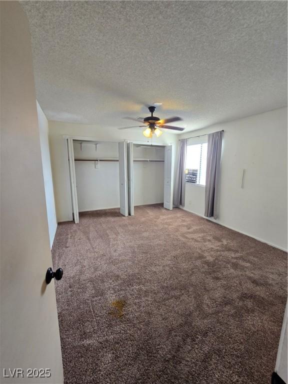 unfurnished bedroom featuring a textured ceiling, carpet flooring, a ceiling fan, and multiple closets