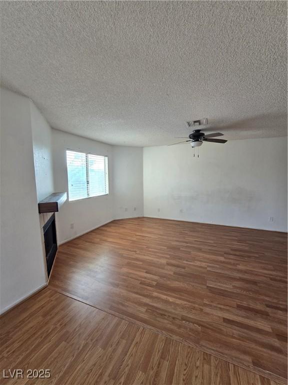 unfurnished living room with visible vents, a tiled fireplace, a ceiling fan, a textured ceiling, and wood finished floors