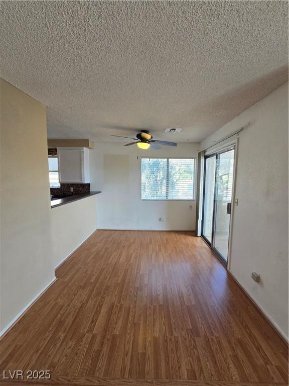 unfurnished living room with visible vents, baseboards, ceiling fan, a textured ceiling, and wood finished floors