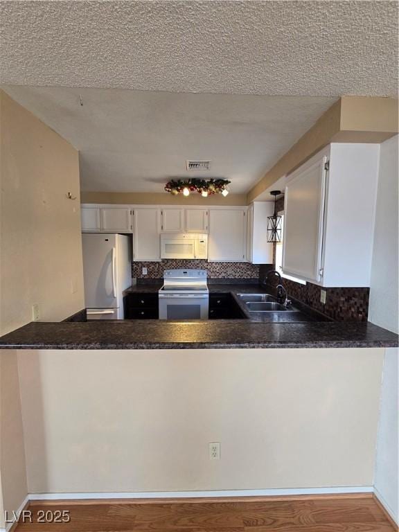 kitchen with tasteful backsplash, white appliances, a peninsula, white cabinetry, and a sink