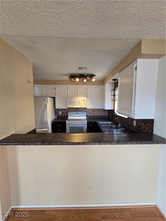 kitchen featuring white appliances, a peninsula, visible vents, decorative backsplash, and a sink