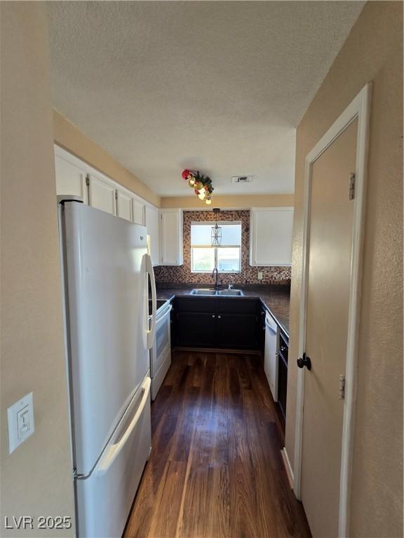 kitchen with white cabinets, white appliances, a sink, and dark countertops