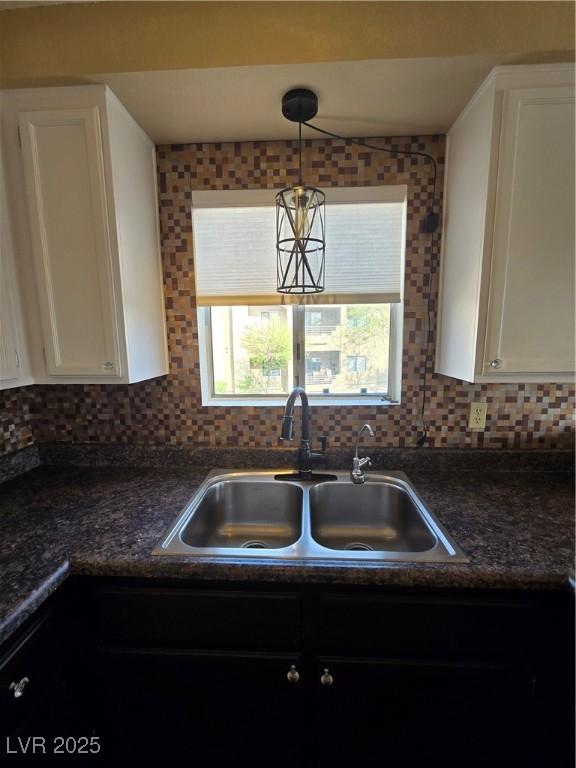 kitchen with a sink, tasteful backsplash, white cabinetry, and dark countertops