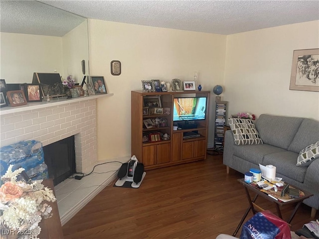 living area with a brick fireplace, a textured ceiling, and wood finished floors