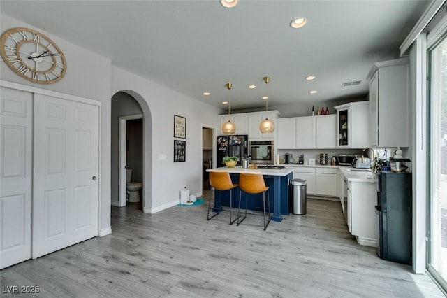 11769 Via Vera Cruz Ct, Las Vegas, NV 89138 - kitchen featuring stainless steel oven, arched walkways, a breakfast bar, light wood-style flooring, and white cabinets