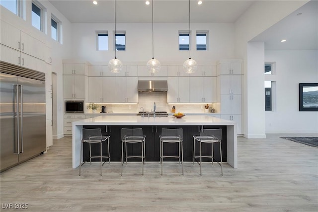 148 Tre Pietre St, Henderson, NV 89011 - kitchen featuring built in appliances, light wood-style flooring, light countertops, exhaust hood, and decorative backsplash