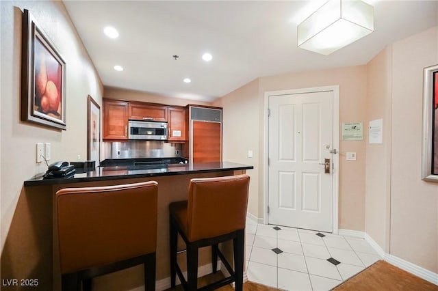 kitchen featuring brown cabinets, stainless steel microwave, dark countertops, recessed lighting, and a peninsula
