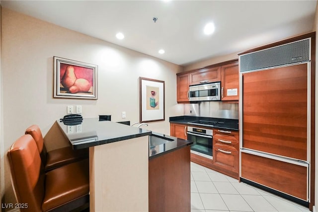 kitchen featuring dark countertops, a peninsula, stainless steel appliances, and brown cabinetry