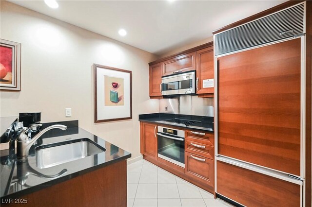 kitchen featuring light tile patterned floors, a sink, stainless steel appliances, dark countertops, and brown cabinets