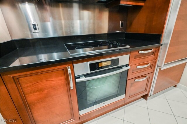 kitchen with brown cabinetry, dark countertops, oven, and black electric cooktop