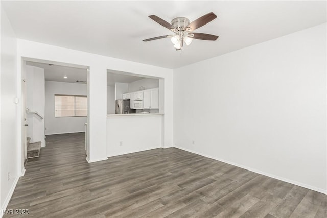 unfurnished living room featuring stairs, dark wood-style floors, baseboards, and ceiling fan
