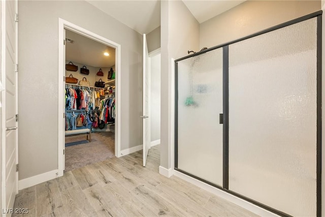 full bathroom with baseboards, a walk in closet, a stall shower, and wood finished floors