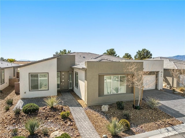 view of front facade featuring a garage, stucco siding, a tiled roof, and decorative driveway