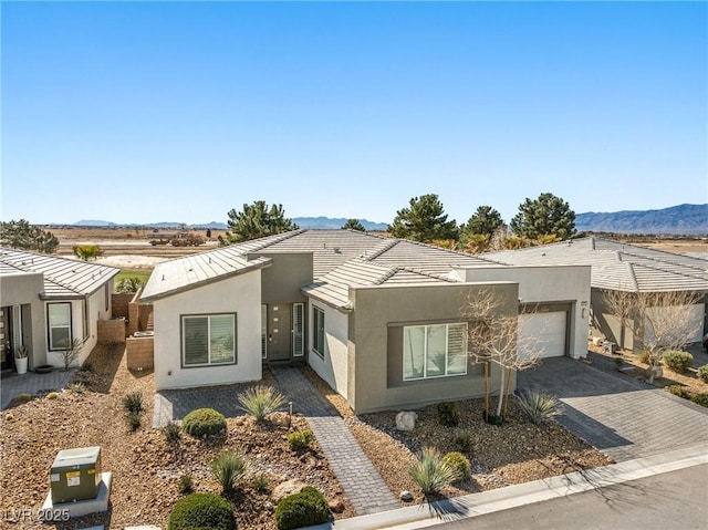 view of front of home with a mountain view, an attached garage, a tile roof, stucco siding, and decorative driveway