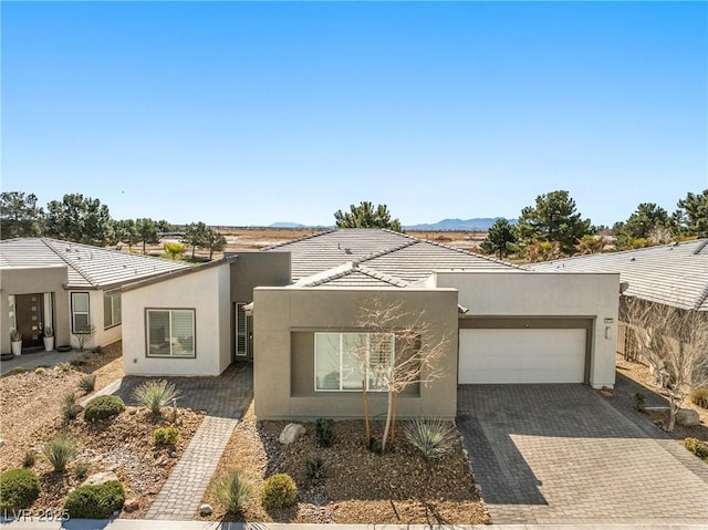 view of front of home featuring an attached garage, a tiled roof, stucco siding, and decorative driveway