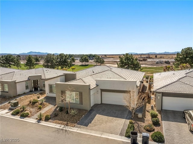 view of front facade with stucco siding, decorative driveway, a tile roof, an attached garage, and a mountain view