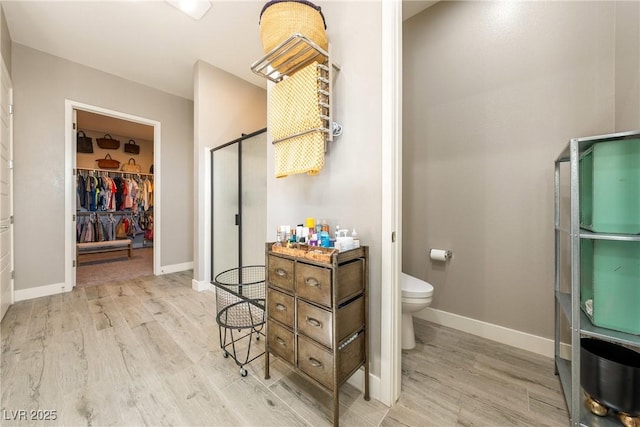 full bath featuring a shower stall, wood finished floors, a spacious closet, and toilet