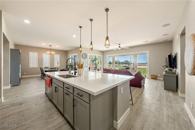 kitchen featuring open floor plan, light wood-style flooring, gray cabinetry, a center island with sink, and a sink