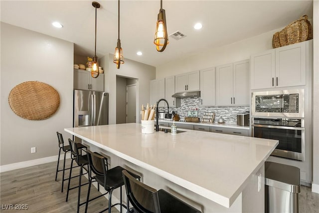 kitchen with visible vents, a sink, appliances with stainless steel finishes, under cabinet range hood, and decorative backsplash