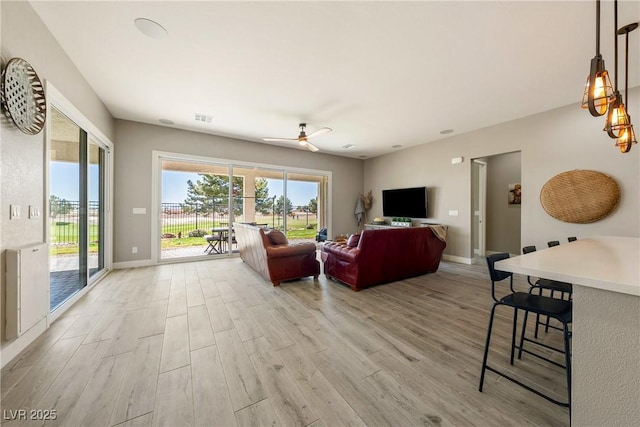living area featuring light wood-style floors, baseboards, a ceiling fan, and visible vents