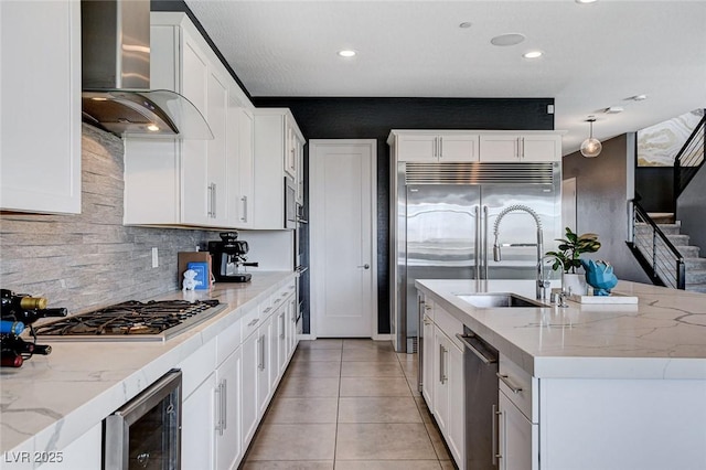 kitchen with wall chimney exhaust hood, appliances with stainless steel finishes, beverage cooler, backsplash, and light tile patterned floors