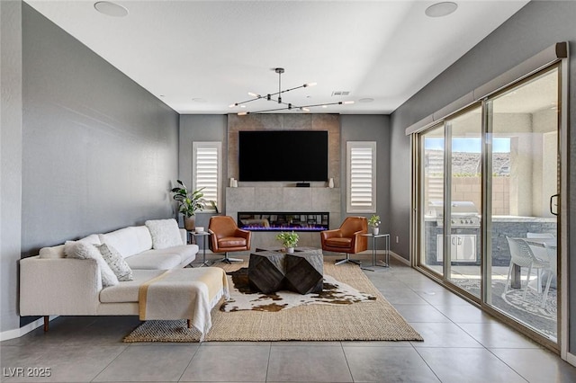 living area with baseboards, tile patterned floors, visible vents, a tiled fireplace, and a notable chandelier