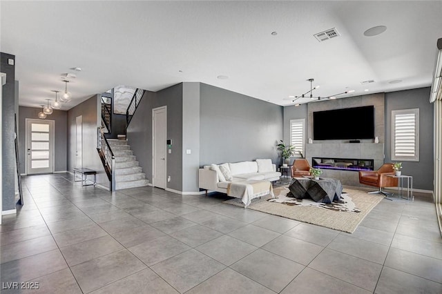 living area with light tile patterned flooring, visible vents, plenty of natural light, stairs, and an inviting chandelier