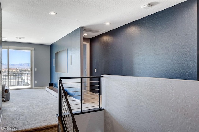 hallway featuring carpet flooring, a textured wall, an upstairs landing, and visible vents