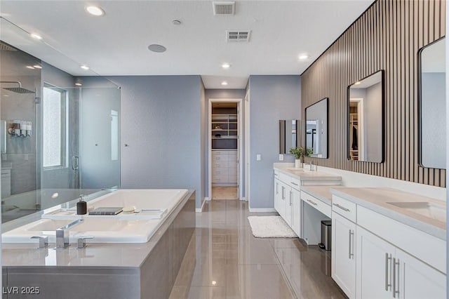 full bathroom with a stall shower, two vanities, a walk in closet, a bath, and visible vents