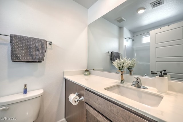 bathroom featuring visible vents, toilet, vanity, and walk in shower