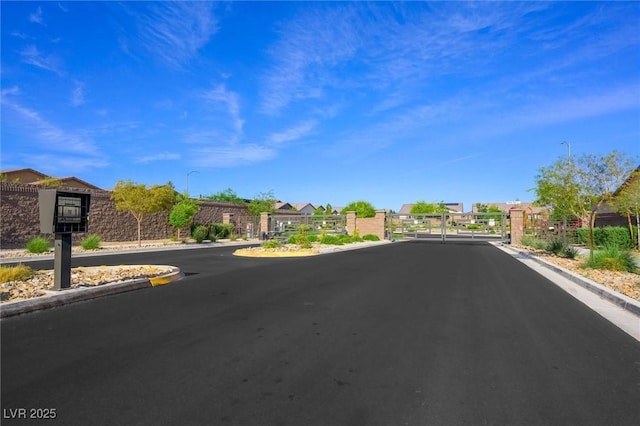 view of street featuring a gate, a gated entry, curbs, and street lights
