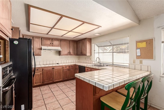 kitchen featuring brown cabinets, a sink, a peninsula, light tile patterned floors, and black appliances