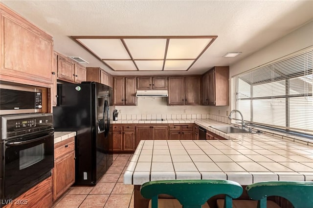 kitchen with range hood, tile counters, a sink, light tile patterned floors, and black appliances