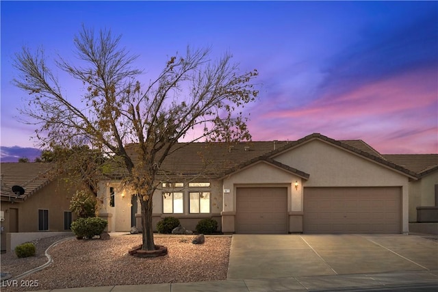 view of front of house featuring a tile roof, a garage, driveway, and stucco siding