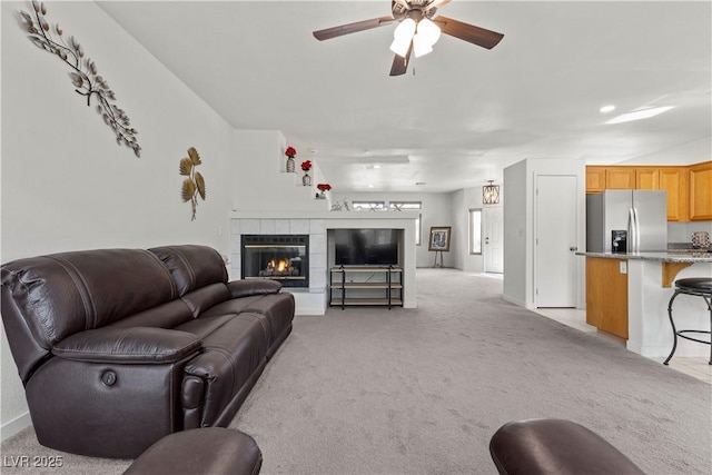 living room with baseboards, ceiling fan, a tiled fireplace, and light carpet